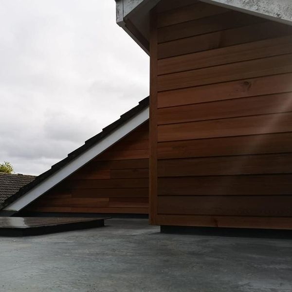 A rooftop view with steeply sloped roofs, featuring wooden siding. The wood panels are set against a cloudy sky, creating a contrast between the dark roof tiles and the warm tone of the wood.